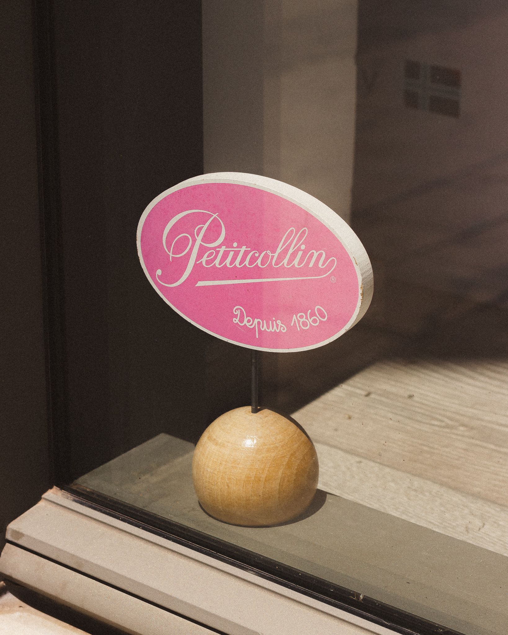 Charming Petitcollin sign in a French window, reflecting vintage elegance.