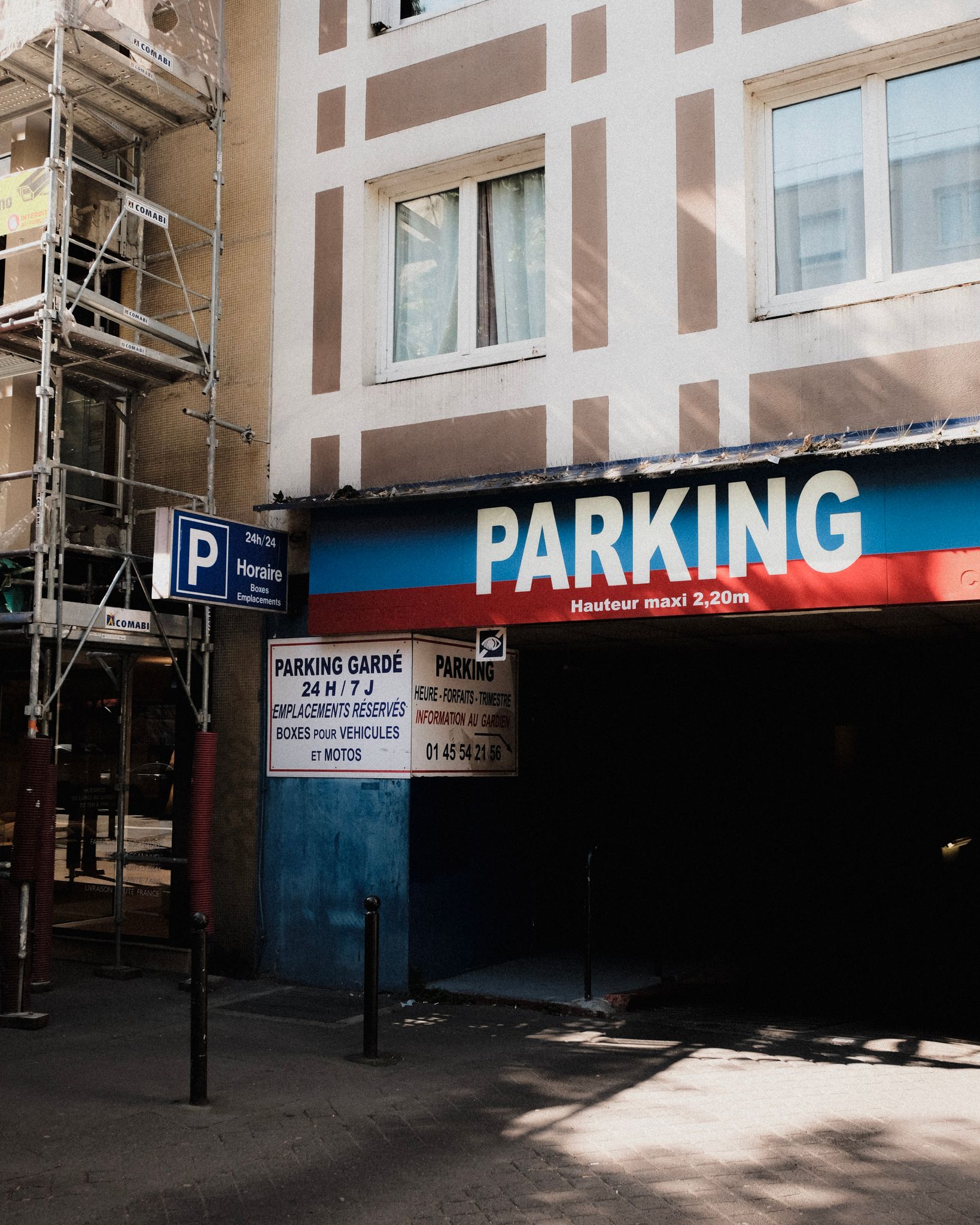 Exterior view of a parking garage entrance with scaffolding on an urban building.