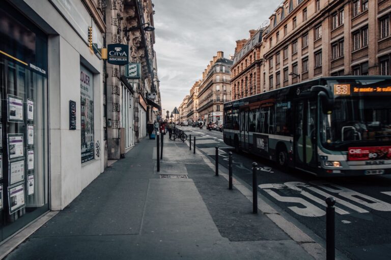 A bustling Paris street scene with a bus, historic buildings, and a quiet sidewalk atmosphere.