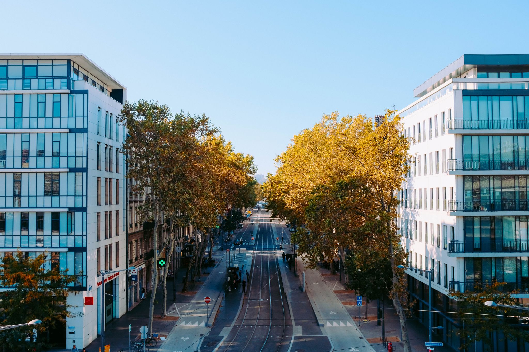 A vibrant urban street scene with contemporary buildings and tree-lined street in daylight.